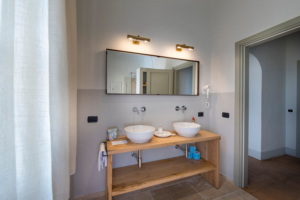 Bathroom at Farmhouse L'Aione, Scansano, with oak vanity, twin vessel sinks, wall-mounted brass sconces, and stone tile floor