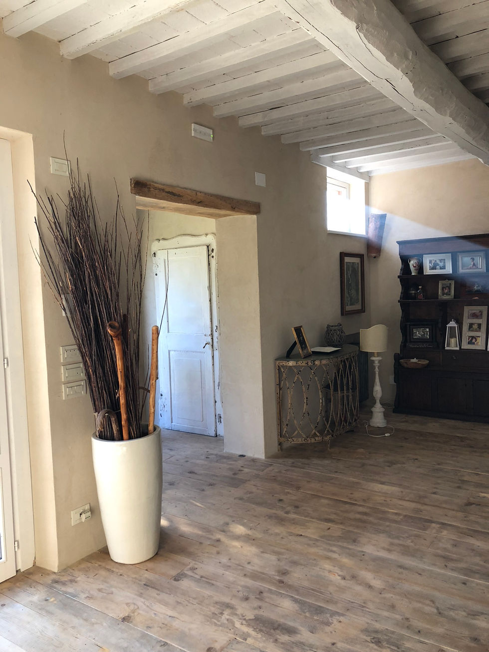 Hallway at Podere Morone Montepulciano with rough plaster walls, exposed timber lintel, distressed white door, and light oak plank flooring