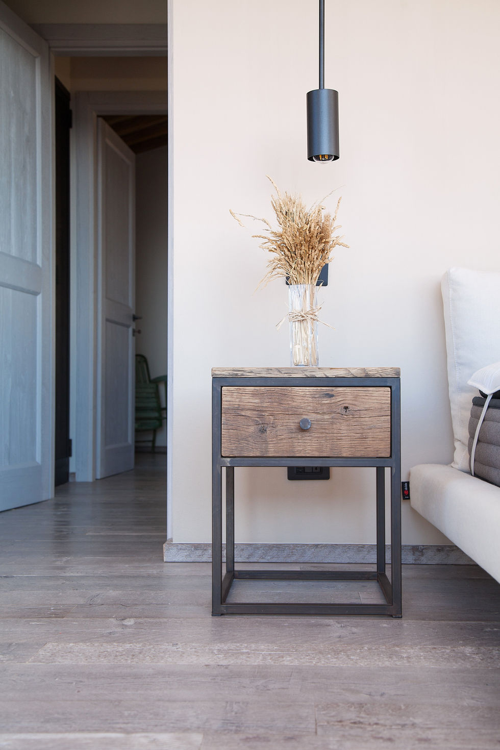 Bedroom nightstand at Villa Bel Colle, Scansano, Maremma, featuring reclaimed wood drawer, dark steel frame, and dried grass vase