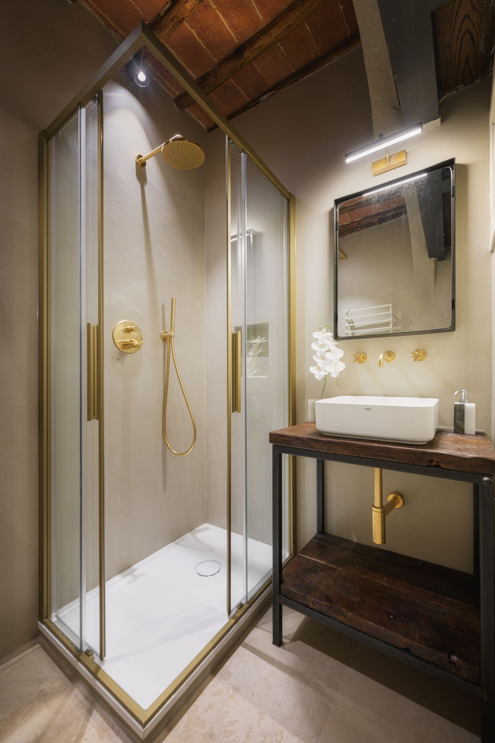 Bathroom with glass shower enclosure, brass fittings, dark wood vanity, white vessel sink, and beige plaster walls in Appartamento Montepulciano, Tuscany