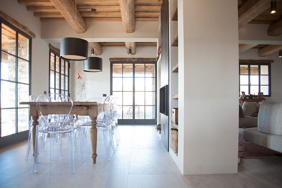 Dining area at Villa Bel Colle Scansano with rustic wood beam ceiling, antique table, ghost chairs, and steel-framed glass doors
