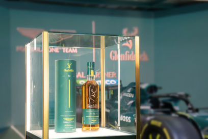 Glenfiddich 威士忌酒瓶和包裝在展示櫃中,背景是 Aston Martin F1 賽車。