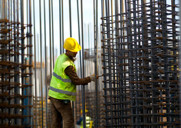Homem trabalhando com barras de aço. Construção com capacete amarelo em Soluvendas.