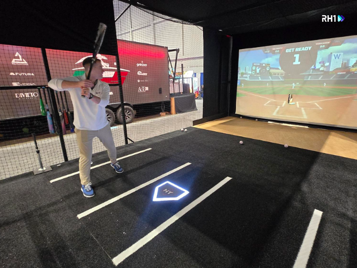 A man swinging a baseball bat in a simulator at IAAPA Expo 2025, showcasing hands-on interactive play