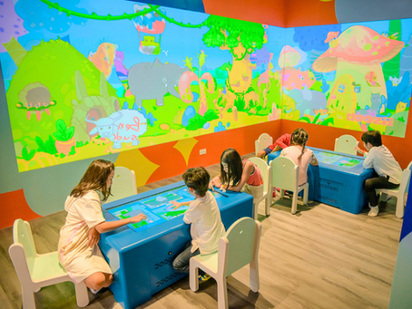 Parents and children drawing together at an interactive table, with their artwork coming to life on the digital animation screen behind them in a family-friendly edutainment zone.