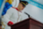 Joven militar en uniforme habla ante micrófono con fondo azul. Colegio Militar Acoolsure.