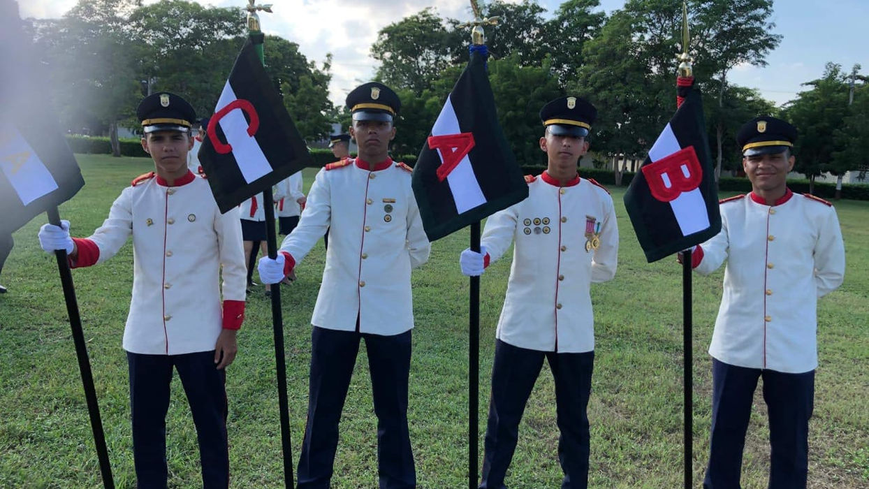 Cuatro hombres uniformados sostienen banderas negras con insignias. Militar, Colegio Militar Acoolsure.