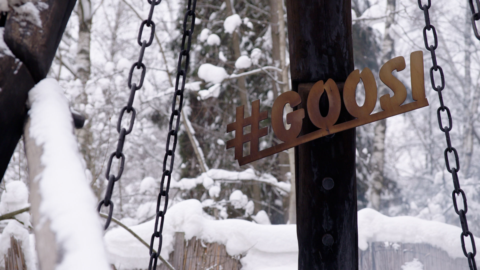 On Sauna Channel, a sign on a wooden beam surrounded by snow at Banya Goosi-Lebedi reads #GOOSI