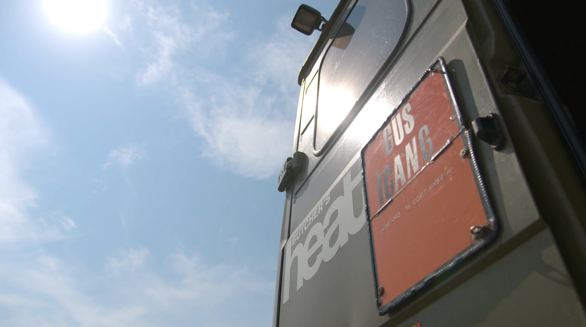 צילום של ערוץ סאונה, מבט למעלה אל החלק האחורי של משאית Butcher's Heat בקופנהגן, דנמרק, עם שלט הכניסה על הדלת הפתוחה ושמיים כחולים שטופי שמש ברקע.