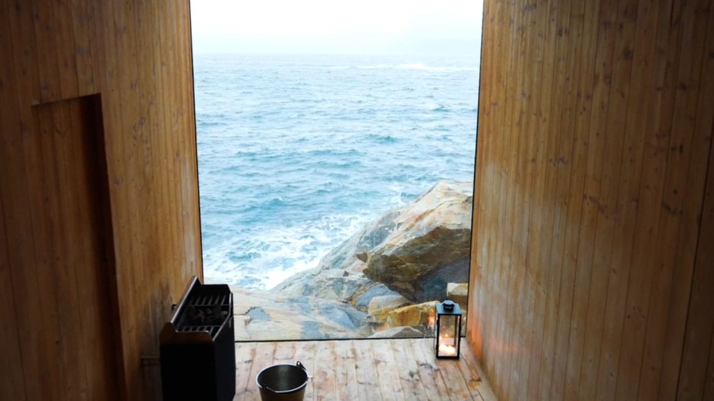 The wooden sauna interior with a floor-to-ceiling window and views of the arctic sea on the Trevarefabrikken episode of Sauna Channel in Lofoten, Norway.