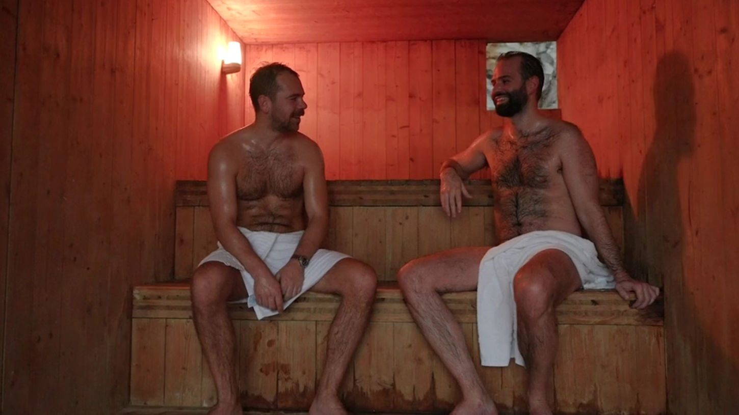 Two men wearing white towels sit down and enjoy the wood sauna at Trevarefabrikken in the Lofoten Islands, Norway on Sauna Channel.