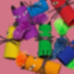 Colourful cardboard tube cats with pom-pom tails and paper whiskers in various hues on a pink background, creating a playful mood.