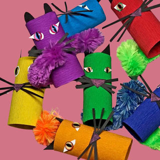 Colourful cardboard tube cats with pom-pom tails and paper whiskers in various hues on a pink background, creating a playful mood.