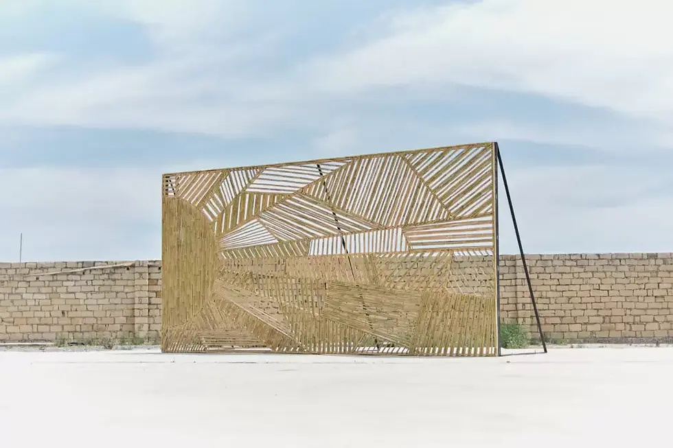 Outdoor installation by Jennifer Douzenel titled Shadow Time, featuring a large bamboo structure with abstract geometric patterns, set against a stone wall and blue sky.