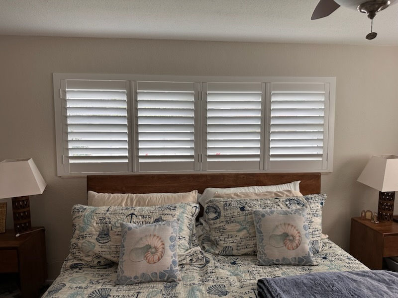 Custom white shutters over a bed