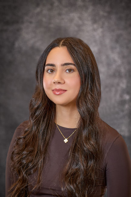 Studio portrait of a woman with long dark brown hair in a brown top, smiling slightly.
