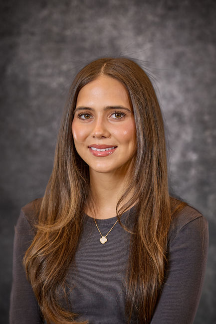 Woman with long brown hair in a dark top, softly smiling in a studio portrait.