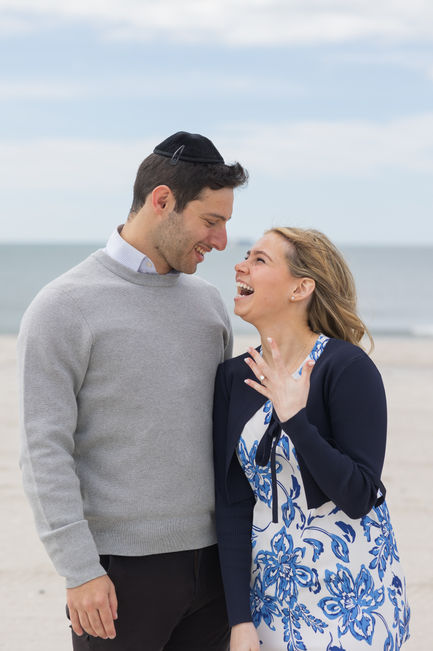 Couple standing on the beach, gazing into each other's eyes with smiles, dressed casually and elegantly.