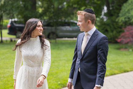 Bride and groom gazing at each other with smiles in a grassy garden area.