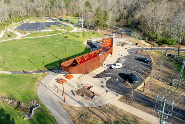 Drone shot of orange structure with grass and trails on left and parking lot on right