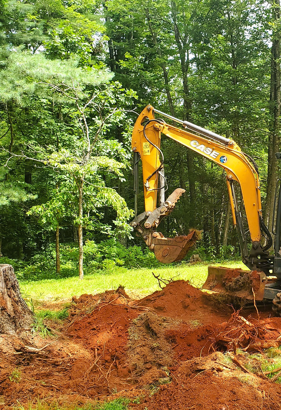 Yellow Case excavator digging a stump out in wooded area.