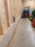 Interior of a wooden garage with stored machinery focusing on foundational concrete wall and pad