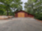 Red wooden detached garage with large light-colored sliding doors. Concrete retaining wall with stairs to the left and a concrete pad in front of doors.