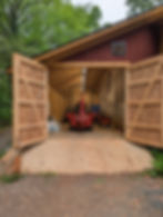 Red tractor inside a wooden addition to a detached garage with large open doors.