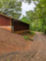 Red detached garage beside a gravel driveway and green forest.