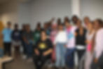Group of smiling young people and an older woman indoors.