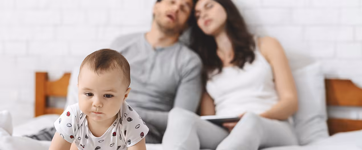 tired parents falling asleep while their baby moves around