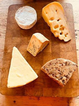 Selection of cheese on a wooden grain end chopping board, cheese include a wedge of Mayfield swiss, its a holey cheese made by Alsop and walker in sussex, it has the texture of an Emmental but tastes more like a Comte. There is a small Baron Bigod Brie from Fen Farm dairy in Norfolk, a small wedge of Colston Basset stilton, some wookey Hole cave aged cheddar that is matured in the caves in somerset and some Sticky Toffee Cheddar, which has, toffee pieces, dates and raisins in this cheeses, its great on a chocolate digestive with toffee sauce drizzed over