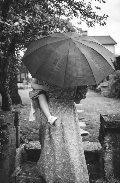 Photo artistique d'une maman portant son enfant sur la hanche et tenant un parapluie dans l'autre main, au cours d'une séance photo famille en extérieur