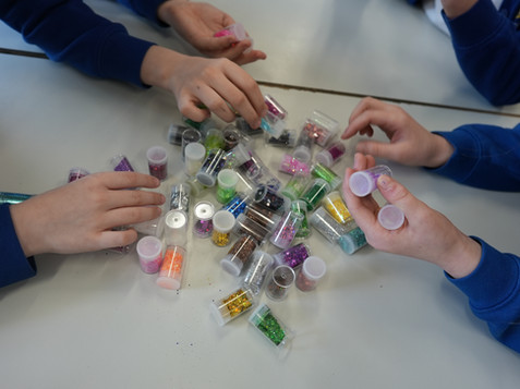 childrens hands choosing little pots of colourful glitter