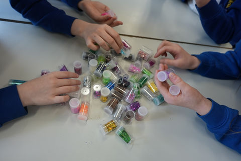 childrens hands choosing little pots of colourful glitter