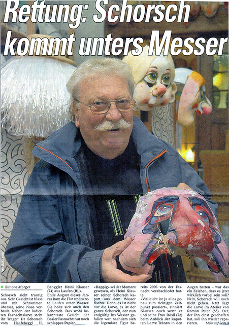 Zeitungsausschnitt aus dem Baslerstab: Heini Klauser mit der "Schorsch" Larve. Ein Foto von Martin Töng, Baslerstab 2007/2008, Basel. Aufgenommen im Larven Atelier Charivari