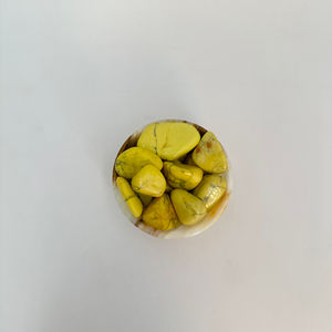 Aerial view of a small stone bowl filled with yellow-dyed howlite. On a white background