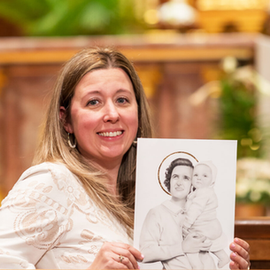 Founder Jennifer sits in the front pew of a church holding a picture of St. Gianna with the altar in the background.