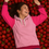 Thumbnail: Smiling woman wearing Strawberry Cream Unisex Hoodie with pink and red color blocks lying on a bed of fresh strawberries enjo