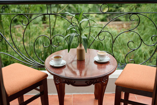 Coffee and tea on a balcony table with garden views.