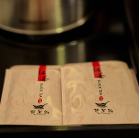 Two packets of black tea on a tray near a kettle.
