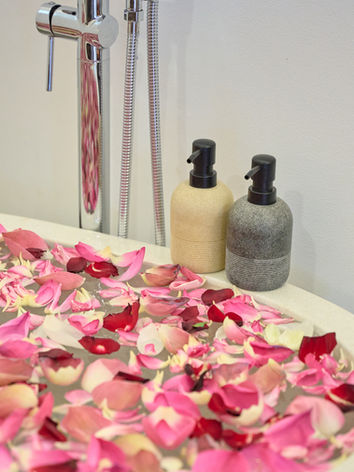 Bathtub filled with pink rose petals next to soap dispensers