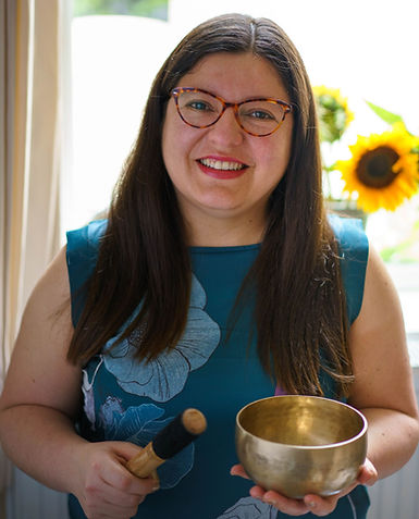 Smiley Pili (woman) wearing glasses, holding a singing bowl. Sunflower in the background.