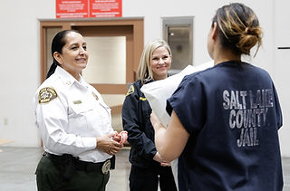 Rosie Rivera in a sheriff’s uniform speaking with a correctional employee and an inmate during the Pillows for Prisoners event at the Salt Lake County Jail.