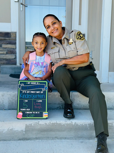 Rosie Rivera in a Sheriff’s Office uniform sitting on porch steps with her granddaughter.