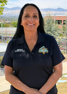 Headshot of Rosie Rivera standing outside wearing a “Re-elect Rosie for Sheriff” shirt.