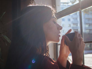 Femme pensive tenant une tasse près d'une fenêtre, moment de pause pendant l'arrêt du tabac