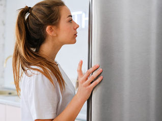 Femme devant un réfrigérateur se demandant pourquoi la faim revient une heure après avoir mangé