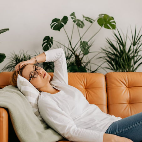 Femme allongée sur un canapé, visiblement fatiguée malgré un moment de repos, illustrant la charge mentale et l'épuisement cognitif.
