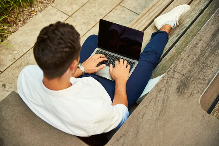 birds eye view of a man typing on his laptop while sitting on a wooden bench